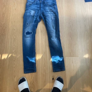 Slim fit jeans Jack & Jones blå 30/32 - Säljer ett par blå slim fit jeans från Jack & Jones, modell Glenn. Jeansen har slitna detaljer och lagade hål framtill för en riktigt snygg och avslappnad look. Klassisk femficksmodell med normal midja och smal passform. Perfekta till sneakers och hoodie. 399kr