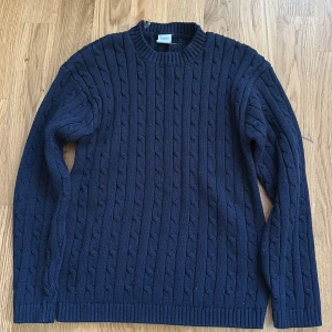 Marinblå stickad tröja från Lindex - Säljer en marinblå stickad tröja från Lindex med snyggt kabelstickat mönster. Tröjan har rund hals, ribbade muddar och långa ärmar. Perfekt för dig som gillar klassisk stil och vill ha något som är både bekvämt och snyggt.