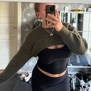 Olivgrön croppad stickad tröja - Säljer en olivgrön croppad stickad tröja med lång ärm. Tröjan har en loose passform och är perfekt att slänga över ett linne eller topp.