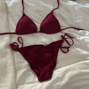 Vinröd calzedonia bikini med snörning - Snygg vinröd bikini med trekantsformad överdel och knyt i sidorna på underdelen. Materialet har en lätt ribbad struktur som ger en cool look. Perfekt för stranden eller poolen i sommar. Bikinin har smala band och är enkel att justera för bästa passform. Har endast använt den en gång🥰🥰