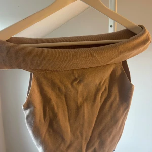Beige stickad axelbandslös klänning - Säljer en beige stickad topp med bred, nedvikt krage som ger en snygg offshoulder-look. Den är axelbandslös och har en mjuk, ribbad struktur som känns både trendig och bekväm. Perfekt för dig som gillar stilrena och enkla plagg med lite edge.