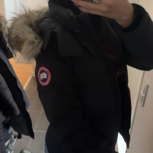 Svart Canada Goose dunjacka med päls - Säljer en svart dunjacka från Canada Goose med fluffig päls runt huvan. Jackan har dragkedja framtill, långa ärmar och en snygg, figurnära passform. Perfekt för kalla vinterdagar och riktigt stilren look. Priset kan diskuteras❤️ postar samma dag som köpt på. 