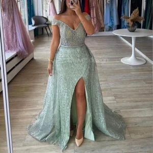 Ljusgrön lång festklänning med pärlor - Oanvänd och helt nytt magisk ljusgrön långklänning från Rever Design med glittriga pärlor och paljetter över hela tyget. Klänningen har offshoulder och v-ringad urringning, samt en snygg slits framtill. Materialet är skimrande och känns lyxigt, perfekt för fester och bröllop. 