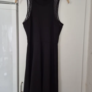 Klänning - Svart klänning från H&M i storlek M. Modellen är ärmlös med mesh-detaljer vid axlarna och har en rund halsringning. Kjolen är lätt utsvängd och klänningen slutar ovanför knäna. Perfekt för dig som gillar enkel och stilren design.