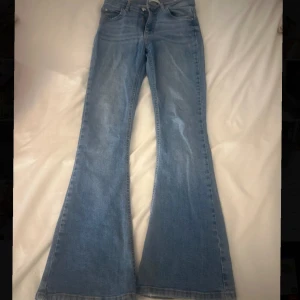 Bootcut ljusblå jeans - Snygga ljusblå bootcut jeans med klassisk femficksdesign och normal passform. Jeansen har en högre midja och är tillverkade i mjukt denimtyg som ger en skön känsla. Perfekta för dig som gillar retrovibbar och vill ha ett par jeans med lite extra sväng i benen.