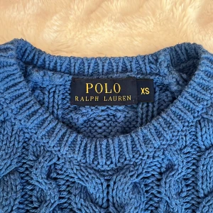 Blå stickad tröja från Polo Ralph Lauren - Säljer en blå stickad tröja från Polo Ralph Lauren i storlek XS💙Tröjan har ett supersnyggt flätmönster och rund halsringning. Långa ärmar och ribbade muddar som ger en klassisk look. Säljer tyvärr då den inte kommer till användning, men perfekt för dig som gillar stilrena och mysiga plagg!💕