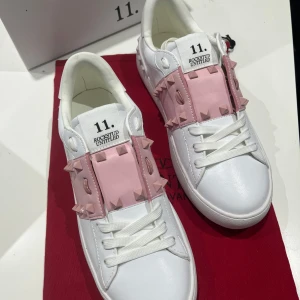 Valentino Rockstud sneakers vit/rosa - Snygga Valentino Rockstud Untitled sneakers i vitt skinn med ljusrosa paneler och ikoniska nitar. Skorna har rund tå, platt sula och vita snören. Perfekt för dig som vill sticka ut med en lyxig och edgy vibe. Märkeslogga på plösen och insidan.
