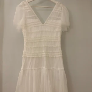 Vit långklänning med volanger och v-ringning - Vit klänning från bubbelroom med prislapp kvar 
