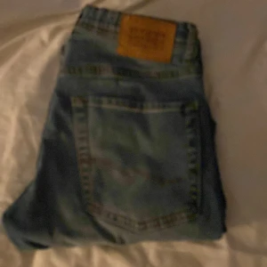 Blå jeans från Jack & Jones, strl 152 - Säljer ett par blå jeans från Jack & Jones i storlek 152. Jeansen har klassisk femficksdesign, slitningar och hål på ena benet för en cool, avslappnad look. De är raka i modellen och har normal passform. Perfekta för dig som gillar streetstyle.