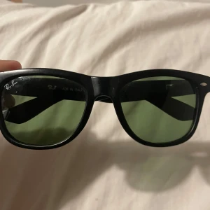 Svarta Ray-Ban solglasögon - Säljer ett par klassiska Ray-Ban Wayfarer solglasögon med svart båge och gröntonade lenser. 