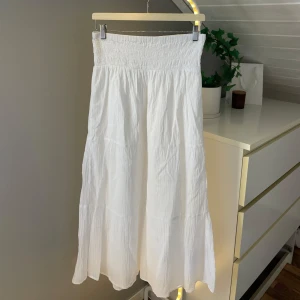 Vit långkjol från Gina Tricot - Säljer en vit långkjol från Gina Tricot i mjuk bomull. Kjolen har en smockad midja som ger en skön och flexibel passform. Kjolen har en pytteliten fläck som ni ser på bild 3. 