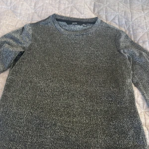 Glittrig svart långärmad tröja från Vera Moda - Säljer en svart långärmad tröja från Vera Moda  med glittrig finish. Tröjan har rund hals och är i ett mjukt, syntetiskt material som ger en cool shimmer-effekt. Perfekt för dig som gillar att sticka ut med lite extra glitter i vardagen.