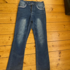 Blå bootcut jeans med stjärndetaljer - Snygga blå bootcut jeans med coola stjärndetaljer på fickorna och kontrastsömmar. Jeansen har en klassisk femficksdesign och är tillverkade i en stretchig mix av bomull, polyester och spandex för skön passform. Perfekt för dig som gillar en lite retro vibe.