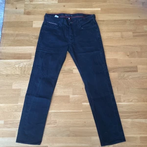 Svarta jeans från Tommy Hilfiger - Snygga svarta jeans från Tommy Hilfiger med klassisk femficksdesign och diskret Hilfiger-logga på bakfickan. Modellen har raka ben och normal passform, med detaljer som knappar och dragkedja framtill. Perfekt för dig som gillar stilrena och tidlösa jeans.