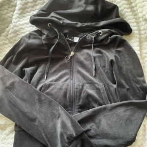 Svart hoodie i velour från Gina Tricot - Mjuk och skön svart hoodie från Gina Tricot i storlek XS. Tröjan är i velour med dragkedja framtill, snörning vid huvan och långa ärmar. Perfekt för chill dagar eller när du vill ha en cozy vibe. Snygg och enkel att matcha med jeans eller leggings.