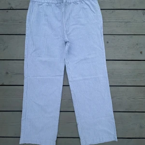 Randiga pyjamasbyxor från Lexington - Snygga ljusblå och vita pyjamasbyxor från Lexington Sleepwear med klassiskt randigt mönster. Byxorna har rak passform, elastisk midja med snörning och en bakficka. Perfekta för chill hemma eller sleepover. Mjukt bomullsmaterial för extra comfort.