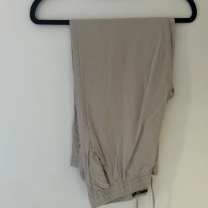 Beige mjukisbyxor från 157, storlek M - Säljer ett par beige mjukisbyxor från 157 i storlek M. Byxorna har resår och snörning i midjan för skön passform. De är tillverkade i mjukt bomullsmaterial och har en avslappnad look som passar perfekt för chill dagar.