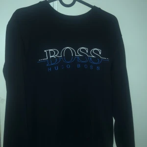 Svart sweatshirt från Hugo Boss - Svart sweatshirt från Hugo Boss med stort broderat BOSS märke på bröstet. Tröjan är bara använd en gång. Tröjan är i storlek S men är liten i storlek så sitter bäst på XS.