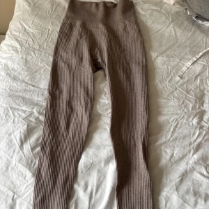 Ribbade bruna leggings XS/S - Säljer ett par ribbade leggings i brun färg med hög midja. De är stickade och har en bred, mjuk linning som sitter skönt. Materialet är stretchigt och passar perfekt för chill eller träning. Tillverkade i Italien och har en slim passform.