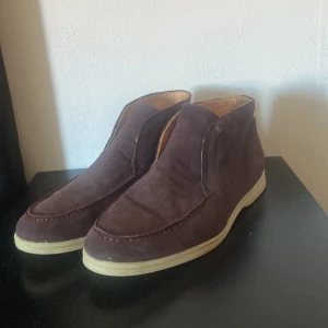 Loro piana Open Walk  - Säljer ett par stilrena boots i mörkbrun mocka med rund tå och kontrasterande vit platt sula. Skorna har en enkel och clean design utan snörning, vilket ger dem en modern vibe. Insidan är ljusbrun och de passar perfekt till jeans eller chinos. Har tyvärr inte original innersula därav det låga priset! Open walks från Loro piana!