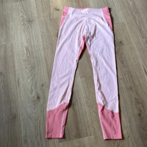 Rosa träningsbyxor  - Snygga leggings i två olika rosa nyanser, med ljusare rosa mitt och mörkare rosa paneler vid midja och benslut. Stretchigt material som sitter tight och följer kroppen, perfekta för träning eller chill. Hög midja för extra komfort och stil. Den är i bra skick och i storlek 158/164