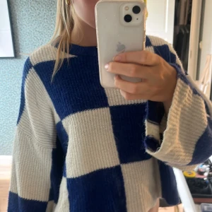 Blåvit rutig stickad tröja Pull&Bear - Säljer en blåvit stickad tröja från Pull&Bear med stora rutiga blockmönster. Tröjan har en loose passform, croppad längd och långa ärmar med breda muddar. Perfekt för dig som gillar en chill och trendig stil. Rund halsringning och mjukt material.