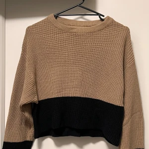 Beige och svart stickad tröja - Säljer en snygg stickad tröja i beige med bred svart kant nedtill. Tröjan har en loose passform och långa ärmar, perfekt för att chilla eller hänga med kompisar. Ribbad rund hals och grovstickad struktur ger en cool vibe.