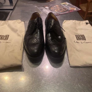 Svarta brogues från Ugo Vasari - Snygga svarta brogues från Ugo Vasari med klassisk snörning och detaljerade perforeringar. Skorna har rund tå och är tillverkade i äkta skinn med lädersula. Perfekt för dig som gillar stilrena och utmärkta skor. Dustbags medföljer. Pris kan diskuteras vid snabb affär. Hör av er vid minsta fundering!