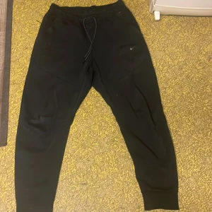 Svarta mjukisbyxor från Nike - Svarta mjukisbyxor från Nike med klassisk logga på benet. Byxorna har snörning i midjan och ribbade muddar vid bensluten. Materialet är mjukt och skönt, perfekt för chill eller träning. Snygg tapered passform och praktiska fickor. litet hål men knappt synligt det är knoppar på dem eftersom dem e andvända ganska mycket men de kan man ta bort med rakaparat gjort det flera gånger på andra byxor köpt nya så så andvänder dem inte mer 