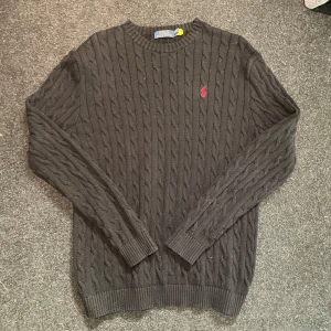 Svart kabelstickad tröja Polo Ralph Lauren - Svart kabelstickad tröja från Polo Ralph Lauren med röd logga. Storlek XL, lite för stor på mig som är 193cm 78kg. Sitter ungefär som L.