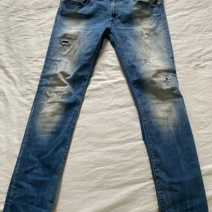 Replay blå slitna jeans, W31 L30 - Säljer ett par blå jeans från Replay med coola slitningar och blekta detaljer på benen. Klassisk femficksmodell med raka ben och slim passform. Perfekt för dig som klär dig grisch.