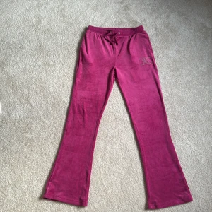 Juicy Couture rosa mjukisbyxor - Säljer ett par snygga rosa mjukisbyxor från Juicy Couture med glittrande JC-logo i strass på ena fickan. Byxorna har bootcut-ben, snörning i midjan och är gjorda i mjuk velour. Perfekta för chill eller när du vill ha en extra glam touch på din outfit. Fans ett litet hål som har blivit sytt, kan se på sista bilden.        Pris kan diskuteras💞