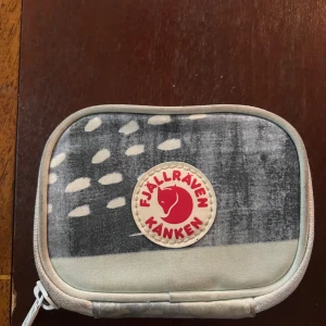 Fjällräven Kånken plånbok med mönster - Plånbok från Fjällräven Kånken med coolt abstrakt mönster i grått, vitt, rosa och svart. Praktisk dragkedja runtom och flera fack inuti för kort och mynt. Tillverkad i slitstark polyester med klassisk Kånken-logga framtill.