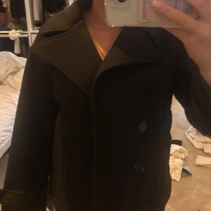 Svart kappa höst jacka  - Säljer en svart kappa med bred krage och dubbelknäppning framtill. Jackan har en rak passform och är tillverkad i ett tjockare material som känns varm. Storlek s/M köpt för 800 kr