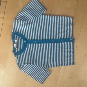 Blåvit randig kofta från Zara - Säljer en kortärmad kofta från Zara med blå och vita ränder. Tröjan har rund hals, knappar framtill och är gjord i mjuk bomull. Perfekt för dig som gillar retrovibbar och vill ha en chill look med lite färg.