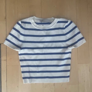 Randig topp från Zara i blått och vitt - Kortärmad topp från Zara med marinblå ränder på vit botten. Modellen är croppad med rund halsringning och ribbad kant. Perfekt för en fräsch och avslappnad stil.