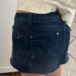Mörkblå jeanskjol - Säljer en mörkblå jeanskjol med rå, fransig kant och klassiska fem fickor. Kjolen har snygga nitar och dekorativa sömmar på bakfickorna. Perfekt för dig som gillar en chill och trendig look. Skriv vid minsta fråga!💕💕