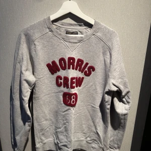 Grå sweatshirt Morris Gents S - Snygg grå sweatshirt från Morris Gents i storlek S. Tröjan har broderad text 'Morris Crew 68' i vinrött framtill och klassisk rund hals. Mjuk bomullskvalitet och långa ärmar gör den perfekt för chill dagar. Passar dig som gillar sportig och avslappnad stil.