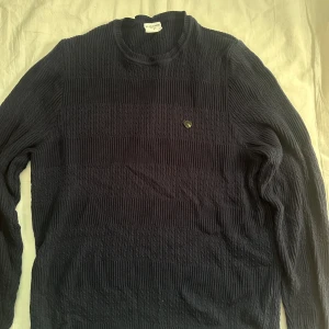 Mörkblå stickad tröja U.S. Polo Assn. - Snygg mörkblå stickad tröja från U.S. Polo Assn. i storlek L. Tröjan har ett diskret emblem på bröstet och ett klassiskt kabelstickat mönster. Rund hals och långa ärmar gör den perfekt för kyliga dagar. Passar dig som gillar stilren och tidlös design.