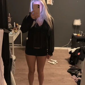 Svart blus med v-ringning och volang - Säljer en svart blus med v-ringad hals och volangdetaljer. Blusen har långärmade, lätt transparenta ärmar med diskret prickigt mönster och elastiska muddar. Luftig och flowy passform som ger en snygg siluett. Perfekt att styla med smycken och jeans.