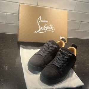 Svarta mocka sneakers Christian Louboutin - Snygga gråa  sneakers från Christian Louboutin i mjuk mocka med klassisk röd sula och grå snörning. Insidan är beige och skorna har en rund tå och platt sula. Har använts fåtall gånger :)