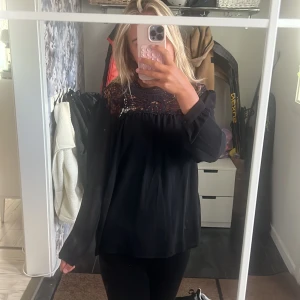 Svart blus med spets från ONLY - Säljer en svart blus från ONLY i storlek 38. Blusen har långärmade, lite transparenta ärmar och en snygg spetsdetalj upptill vid halsen och axlarna. Den har en loose passform och är perfekt för dig som gillar stilrena detaljer och lite romantisk vibe.