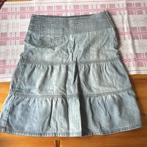 Jeanskjol med volanger från Vero Moda - Säljer en ljusblå jeanskjol från Vero Moda med volangdetaljer och dekorativ ficka bak. Kjolen har en normal passform och är sydd i mjukt jeanstyg. 