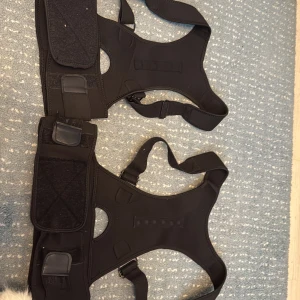 Svart träningsväst med justerbara band - Svart väst med sportig design och breda axelband, perfekt för träning. Västen har justerbara remmar och bred kardborreknäppning runt midjan för extra stöd. Materialet är syntet och ger en flexibel passform. Snygg och funktionell för dig som vill ha stabilitet under aktivitet. Pris per st , köpte för 500kr/st säljer pga intet behov av det längre 