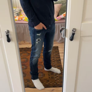 Mörkblå Replay Anbass - Säljer ett par mörkblå Anbass med snygga slitningar och distressed detaljer på benen. Modellen är slim fit med normal passform och klassisk femficksdesign. Jeansen har en midwaist och är gjorda i jeansmaterial med lite stretch för extra komfort.