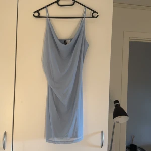 Ljusblå kortklänning från Divided - Säljer en ljusblå kortklänning från Divided by H&M i storlek S. Klänningen har en snygg draperad front och är tillverkad i mjuk polyester. Perfekt för dig som gillar stilrena och enkla plagg med modern touch. Aldrig använd 