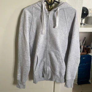 Russemerch hoodie - Ljusgrå hoodie från Russemerch i storlek S. Tröjan har huva med snörning, två fickor fram och hel dragkedja. Mjuk och skön bomullsmix, perfekt för chill dagar. Långärmad och med ribbade muddar vid ärmslut och nederkant. Enkel och stilren design. Fraktar samma dag hela vecka 34🤩