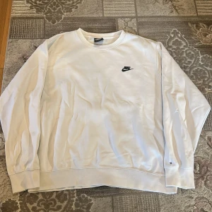 Vit sweatshirt från Nike i storlek L - Vit sweatshirt från Nike med svart logga på bröstet. Tröjan har rund hals, långa ärmar och är tillverkad i mjuk bomull och polyester. Enkel och clean design som funkar till jeans eller joggers. Perfekt för chill dagar eller när du vill ha en stilren look.