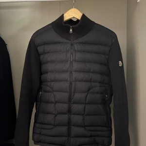 Moncler Cardigan  - Snygg cardigan utan luva från Moncler med quiltad framsida och ribbad krage.  Materialet är en mix av dun och polyester, perfekt för kyliga dagar. Stilren och tidlös design som funkar till många outfits. Säljer åt min kille som har köpt en ny. Storlek XL men fungerar lika bra som L.  Fler bilder finns. Pris kan diskuteras🤩