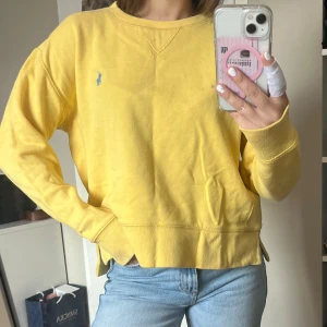 Gul sweatshirt från Polo Ralph Lauren - Säljer en gul sweatshirt från Polo Ralph Lauren i storlek M (barnstorlek, passar bra på mig som är en xs/s). Tröjan har ett blått broderat logomärke på bröstet, rund hals och långa ärmar. Aldrig använd.